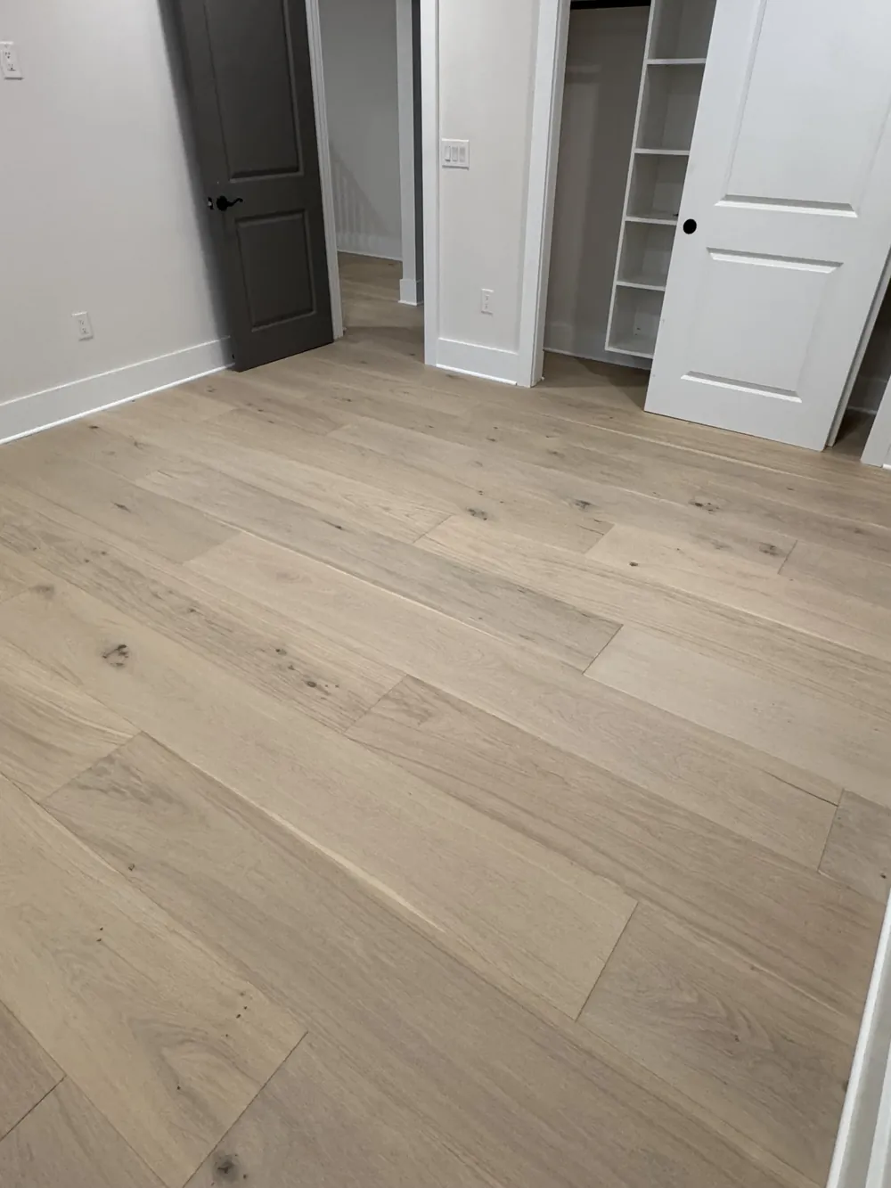 Wide-plank hardwood flooring laid through a doorway toward a closet and hallway